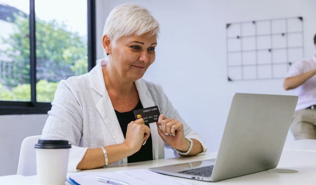 Senior woman consumer holding credit card and laptop buying online at home. Woman shipping online